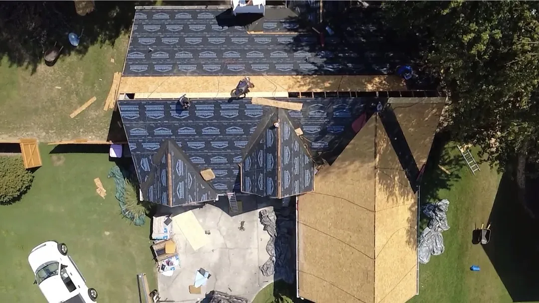 The same roof from above mid-job: bare decking on one section, synthetic underlayment across the rest, and crew working along the ridge.