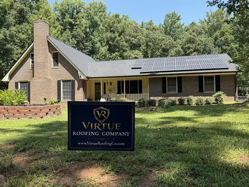 The finished brick ranch home from the front lawn, solar panels on the roof and a Virtue Roofing Company yard sign in the grass.