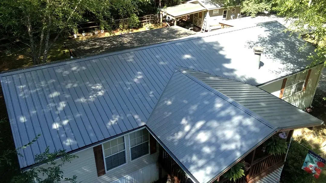 The home with a new gray ribbed metal roof, panels running from ridge to eave in dappled shade.